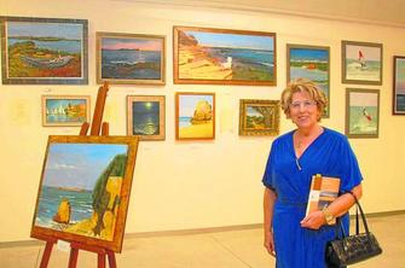María Jesús Rodríguez posa con su libro delante de varios de sus cuadros que forman parte de la exposición.