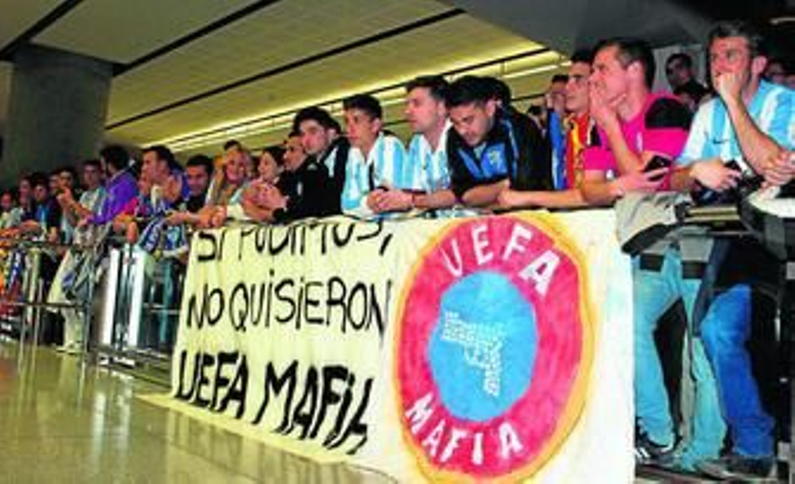 Decenas de seguidores del Málaga reciben al equipo en el aeropuerto con una pancarta contra la UEFA.