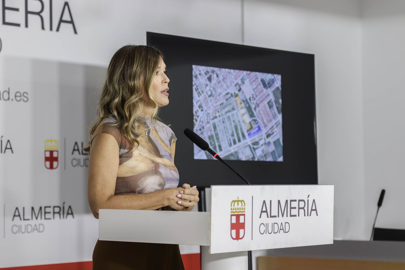 La portavoz municipal del PP en rueda de prensa. En la pantalla, plano del solar cedido