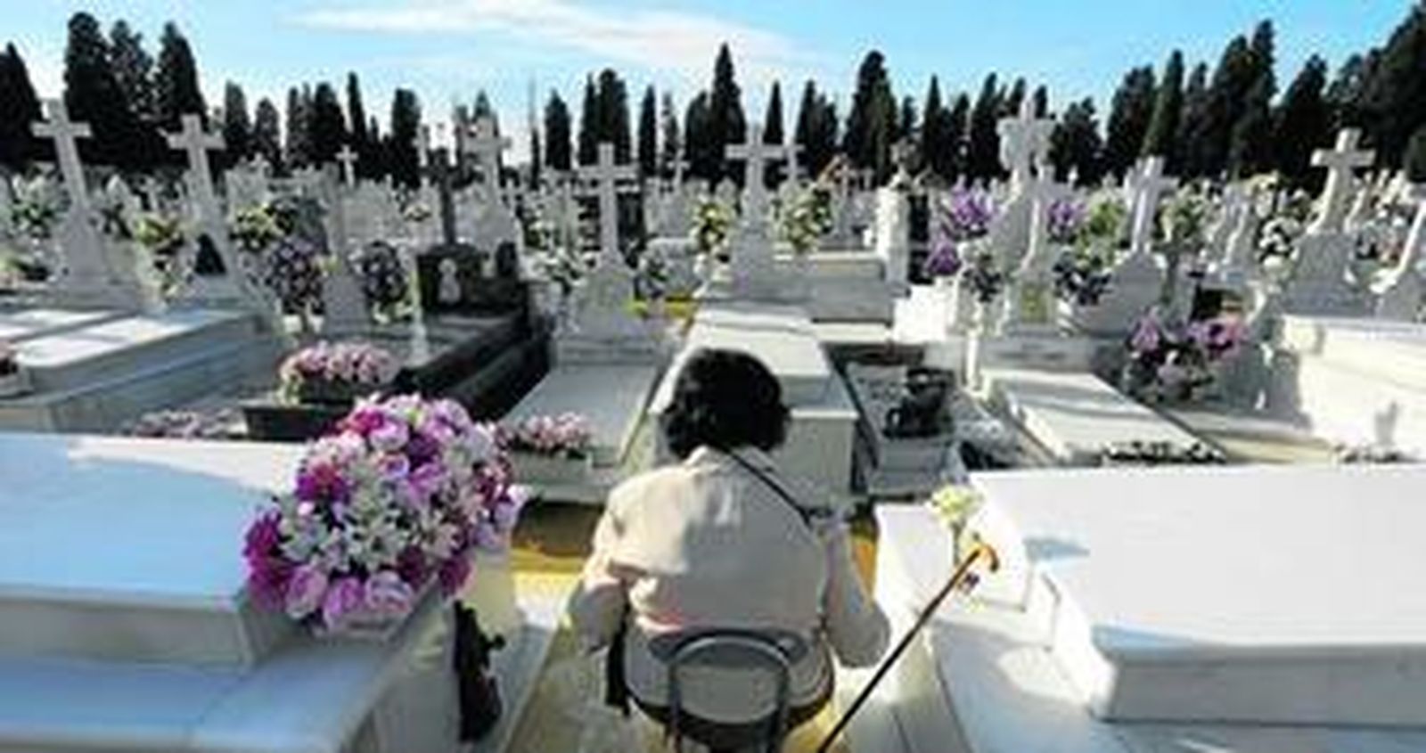 Una mujer sentada frente a una tumba en la inmensidad del camposanto sevillano.