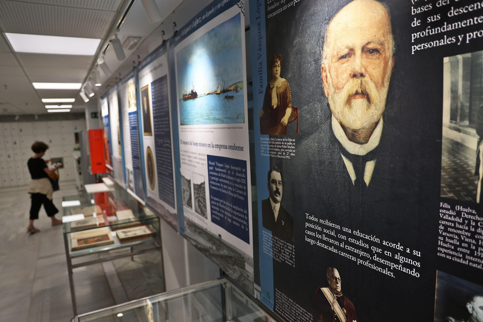 Un conocido retrato de Manuel Vázquez López, en primer término, entre los paneles junto a los ejemplares expuestos en el vestíbulo de la Biblioteca Provincial de Huelva.