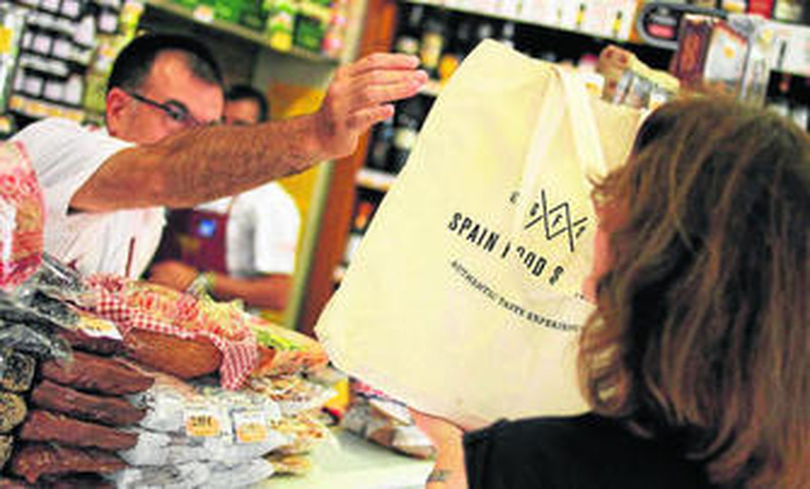 Un trabajador de una tienda de ultramarinos atiende a una turista.
