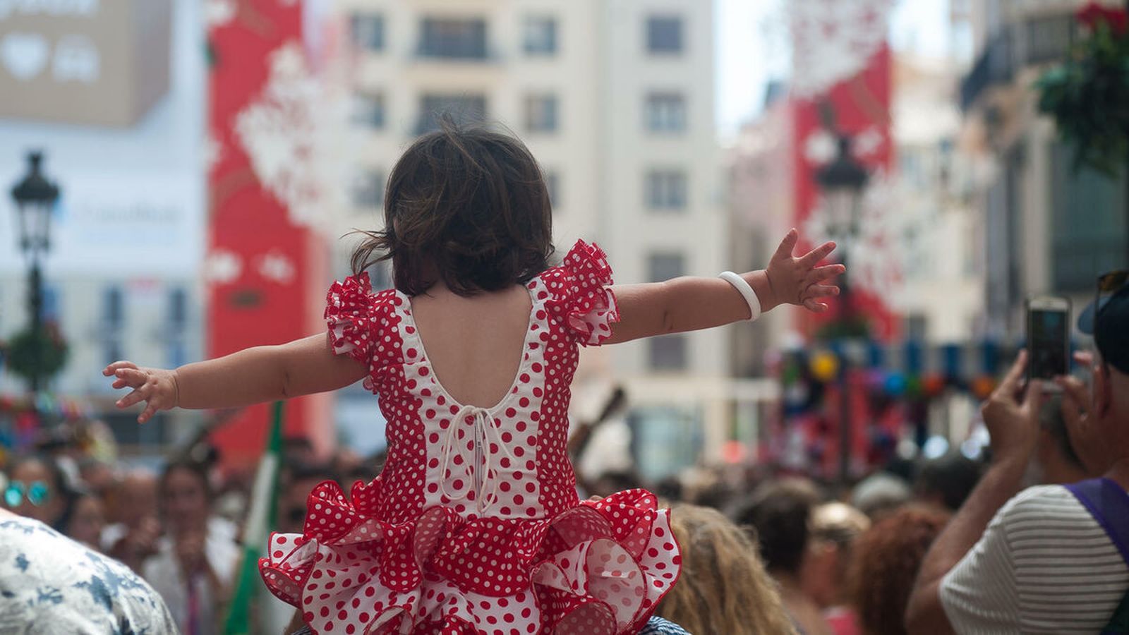 Una niña, vestida de gitana, a hombros de su padre en la Feria de Málaga.