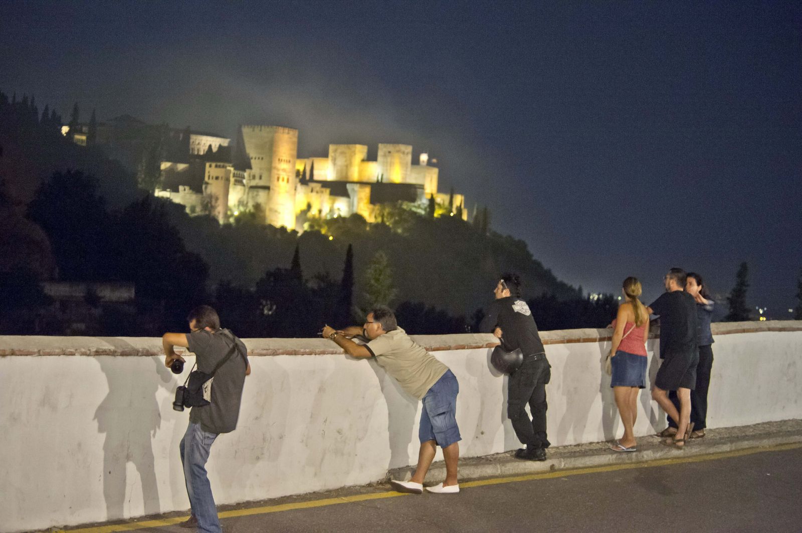 Varios turistas contemplan la Alhambra iluminada por la noche