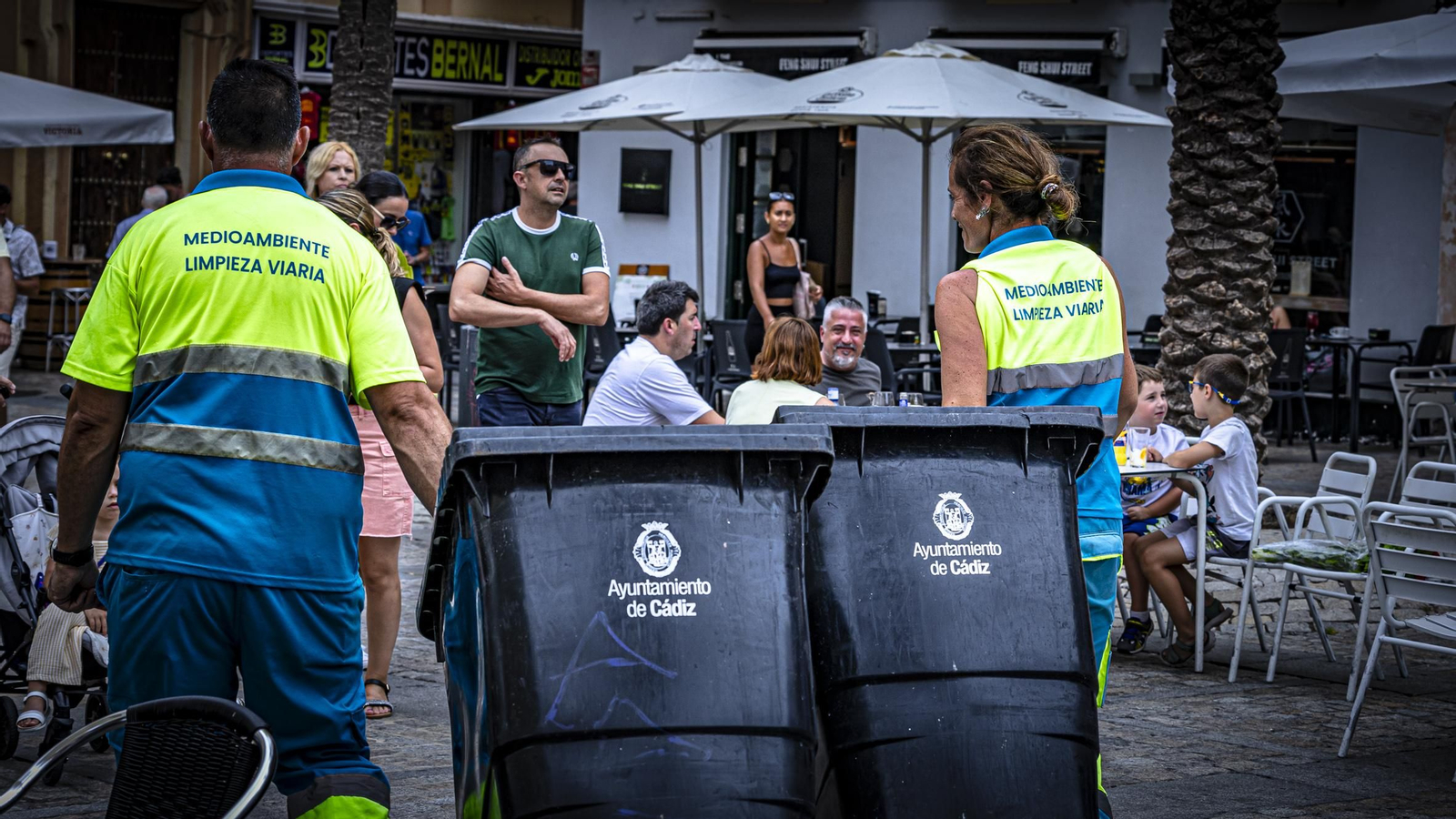 Operarios de limpieza cargan con bidones de basura.