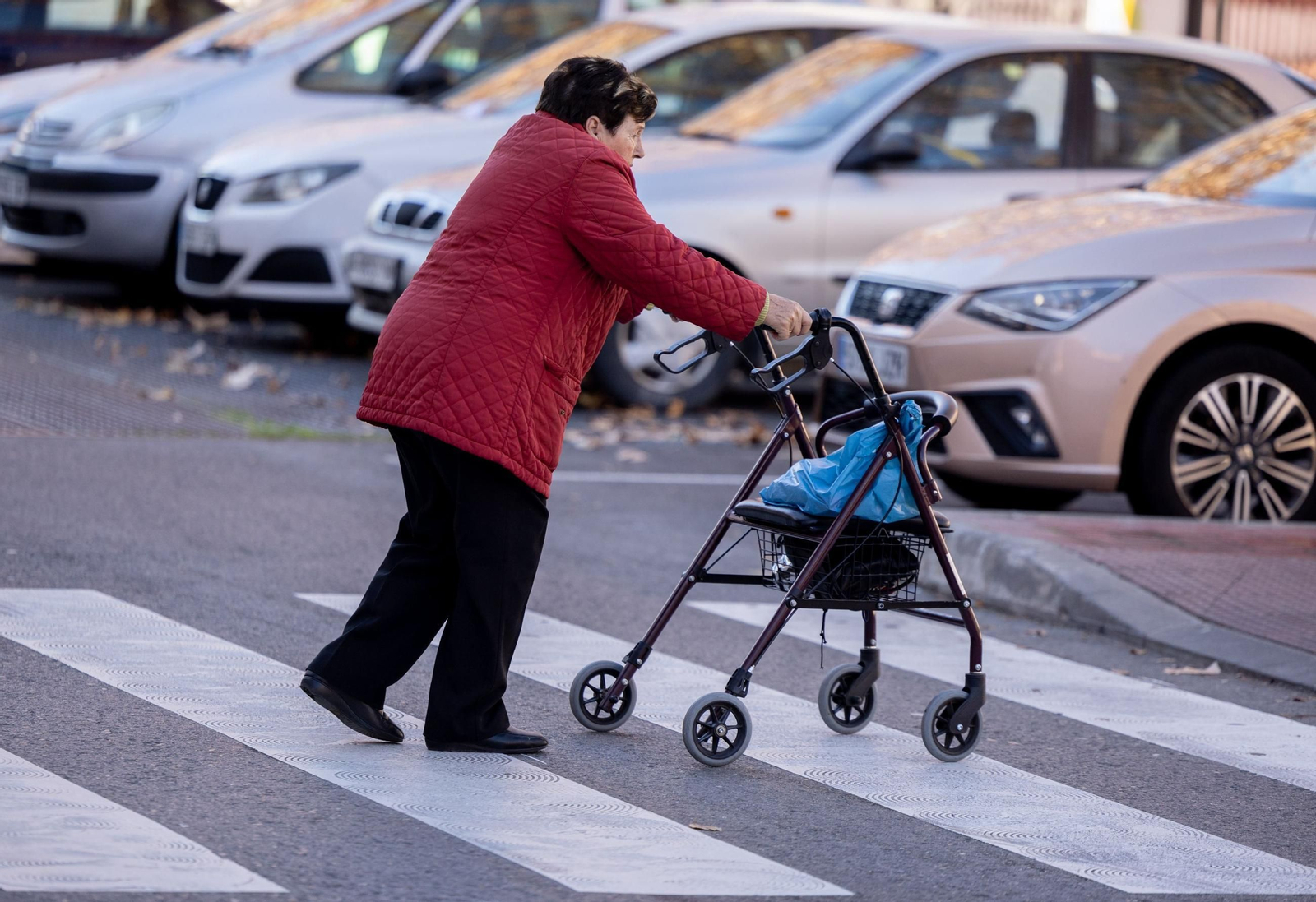 Una mujer de avanzada edad cruzando un paso de peatones con su andador.