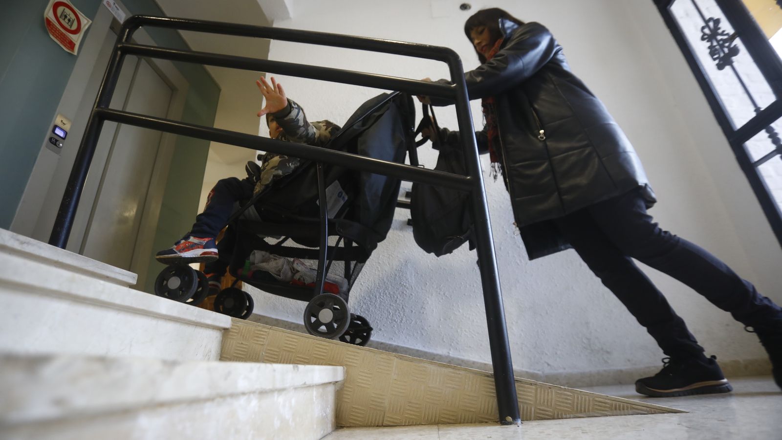 Una mujer sube con el carrito de su hijo en una rampa.
