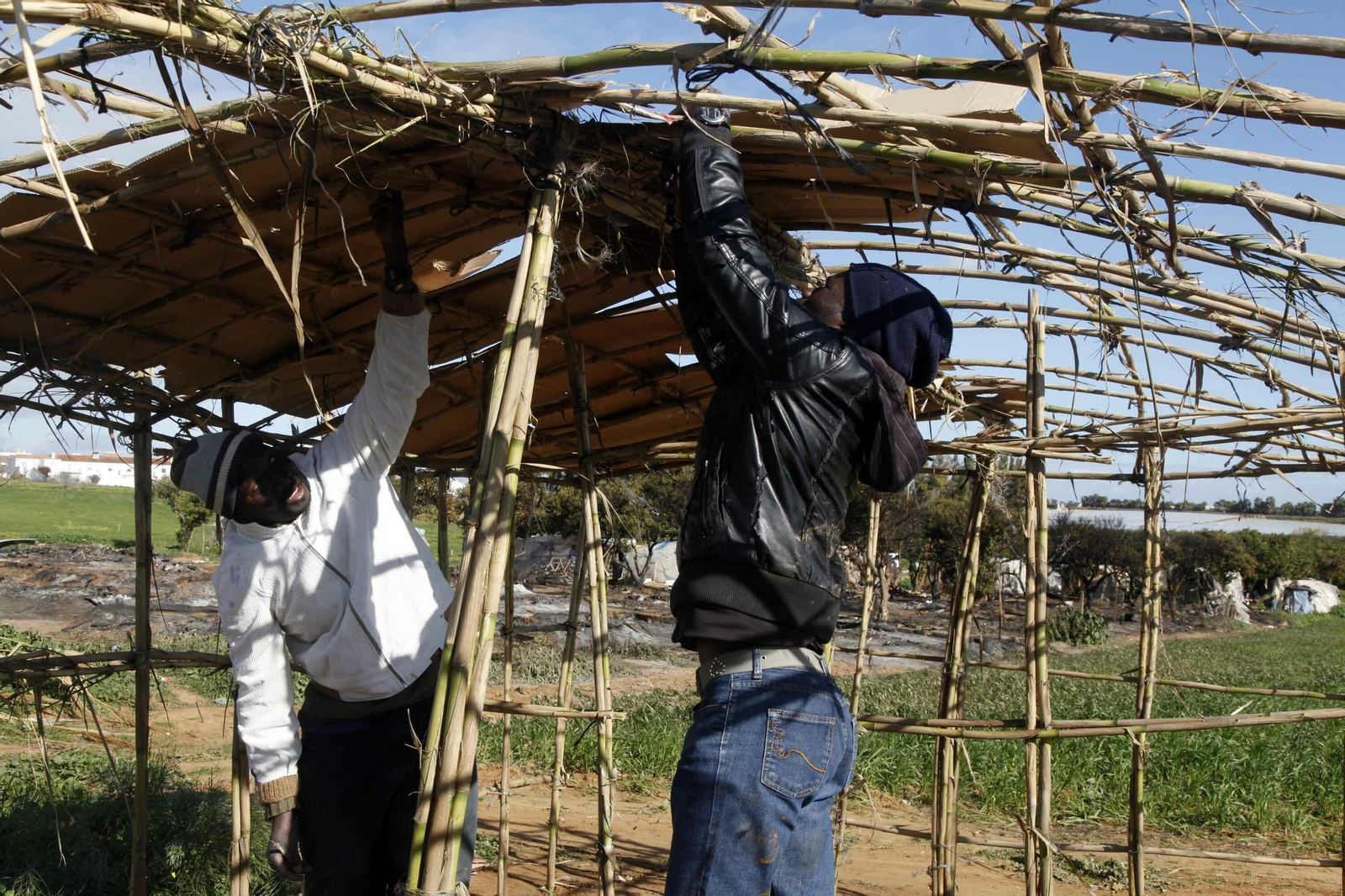 Dos inmigrantes construyen una chabola tras el incendio de un asentamiento.