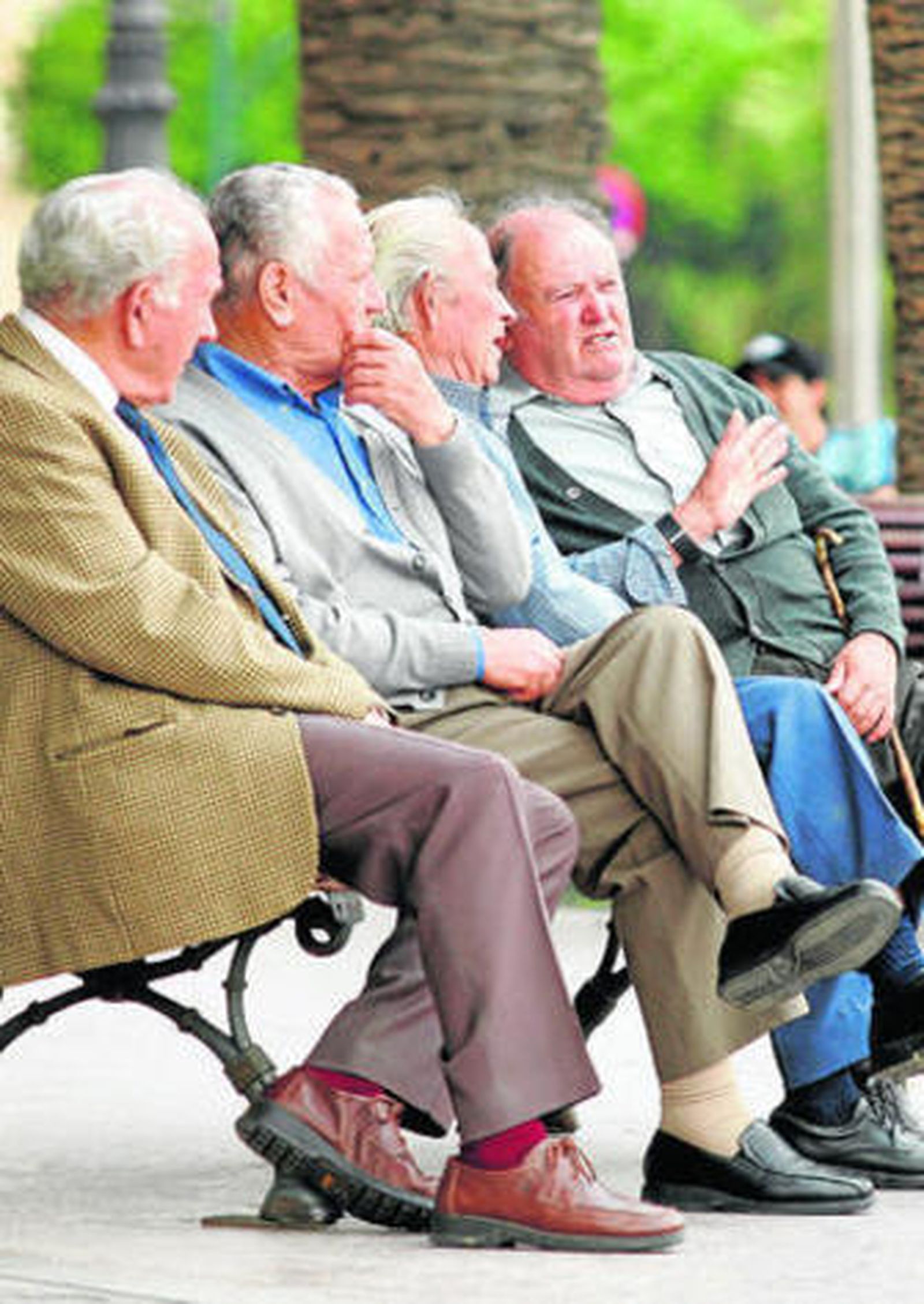 Varias personas mayores sentadas en un banco en la Plaza de la Marina.