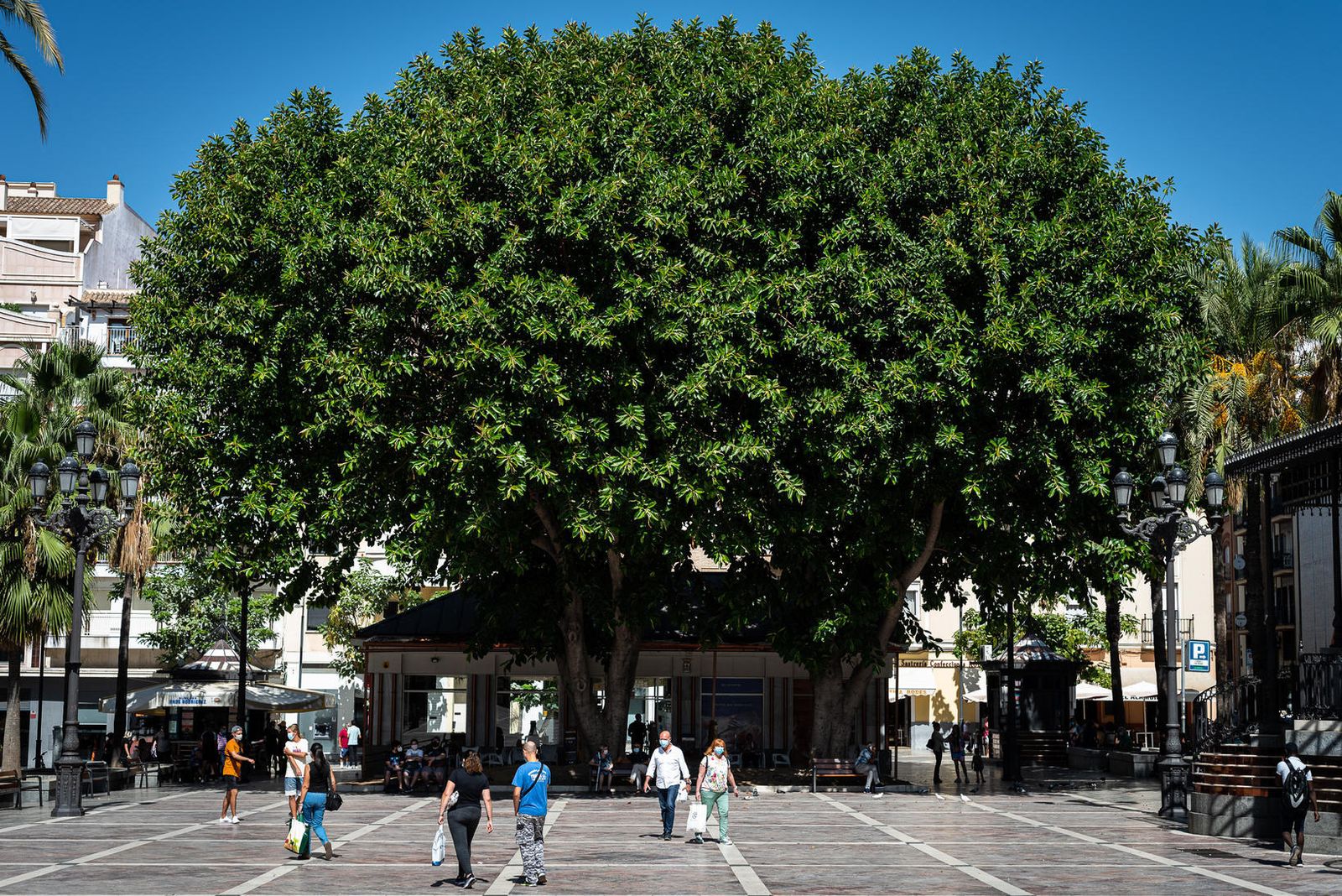 Varios onubenses con bolsas de hacer la compra paseando por la Plaza de las Monjas de la capital