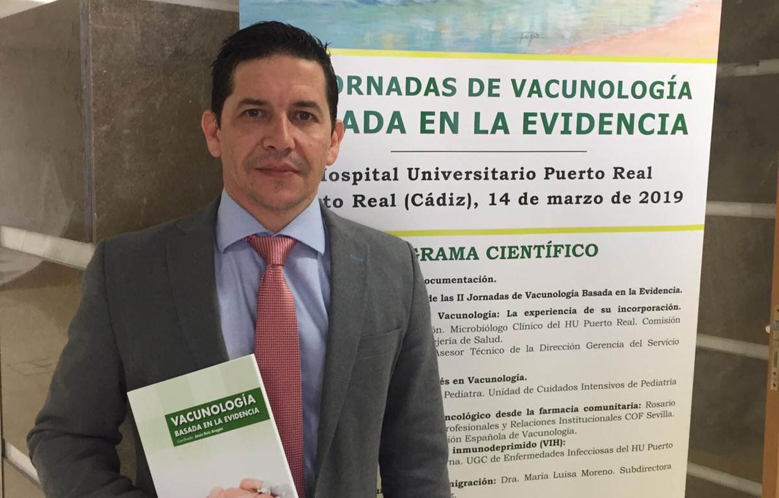 D.C. Jesús Ruiz Aragón ante el cartel de las Jornadas de Vacunología Basada en la Evidencia, en el Hospital de Puerto Real.