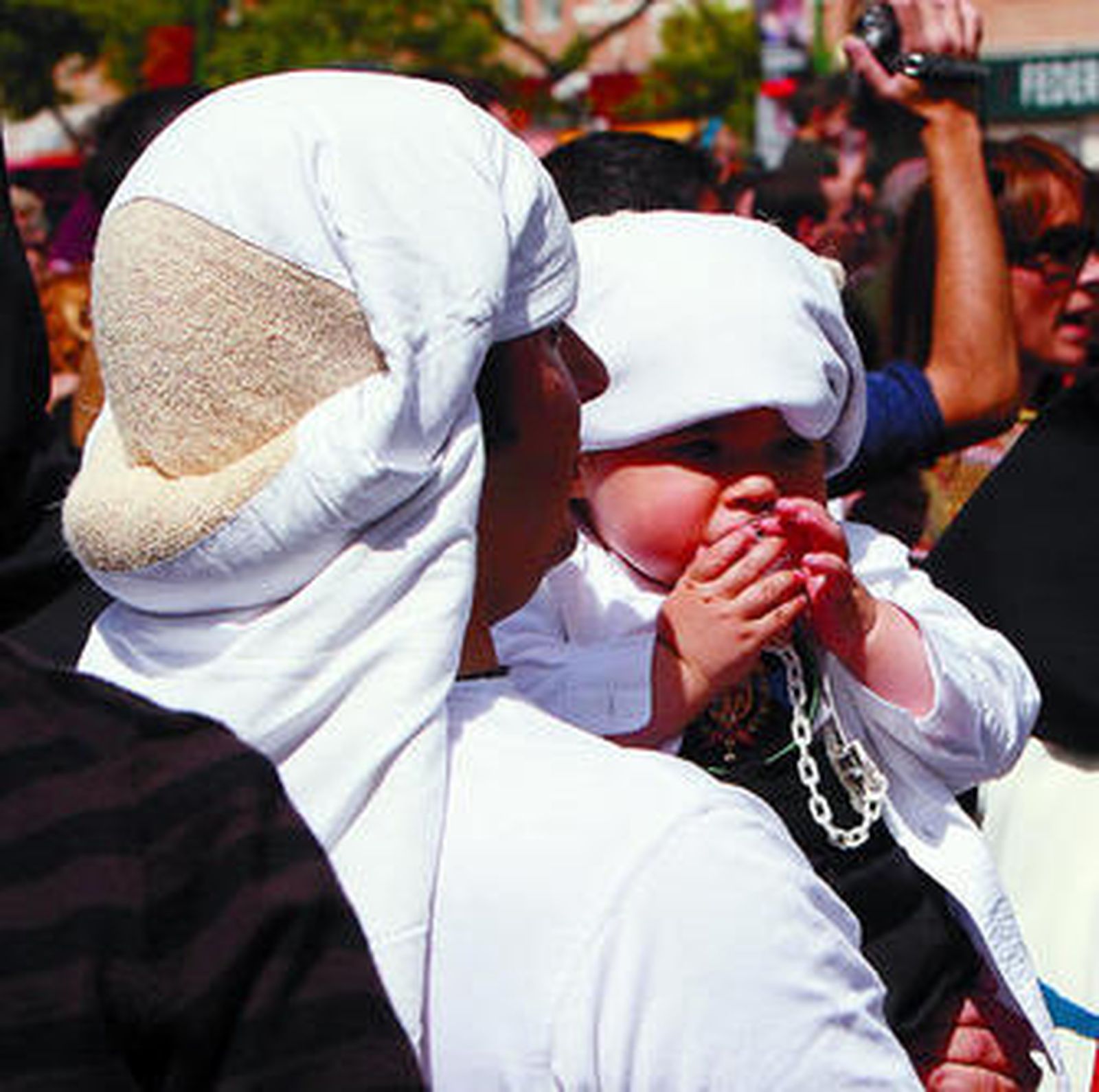 Un niño vestido de costalero en brazos de su padre.