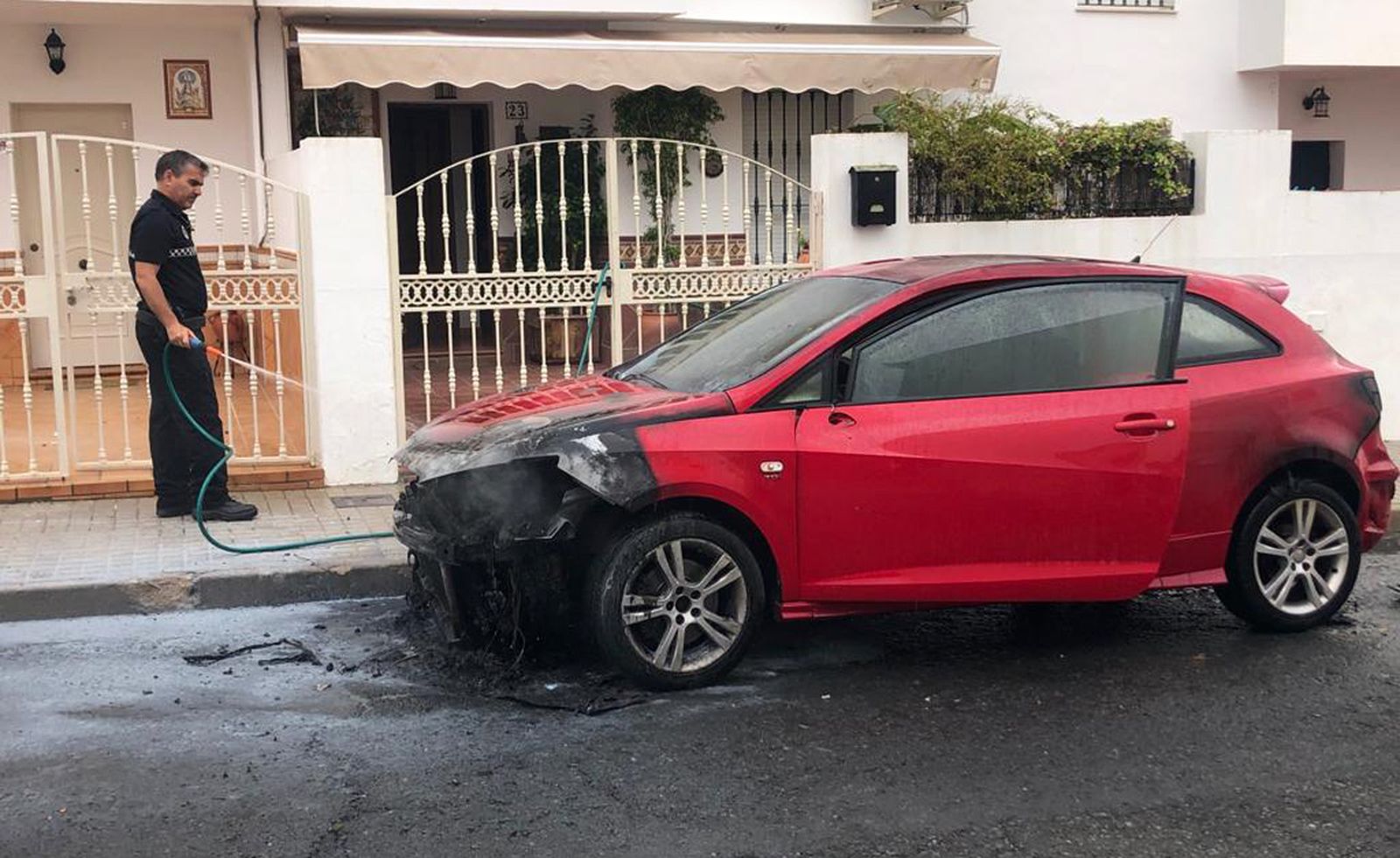 Un agente de la Policía Local combate el fuego con una manguera de agua facilitada por los vecinos