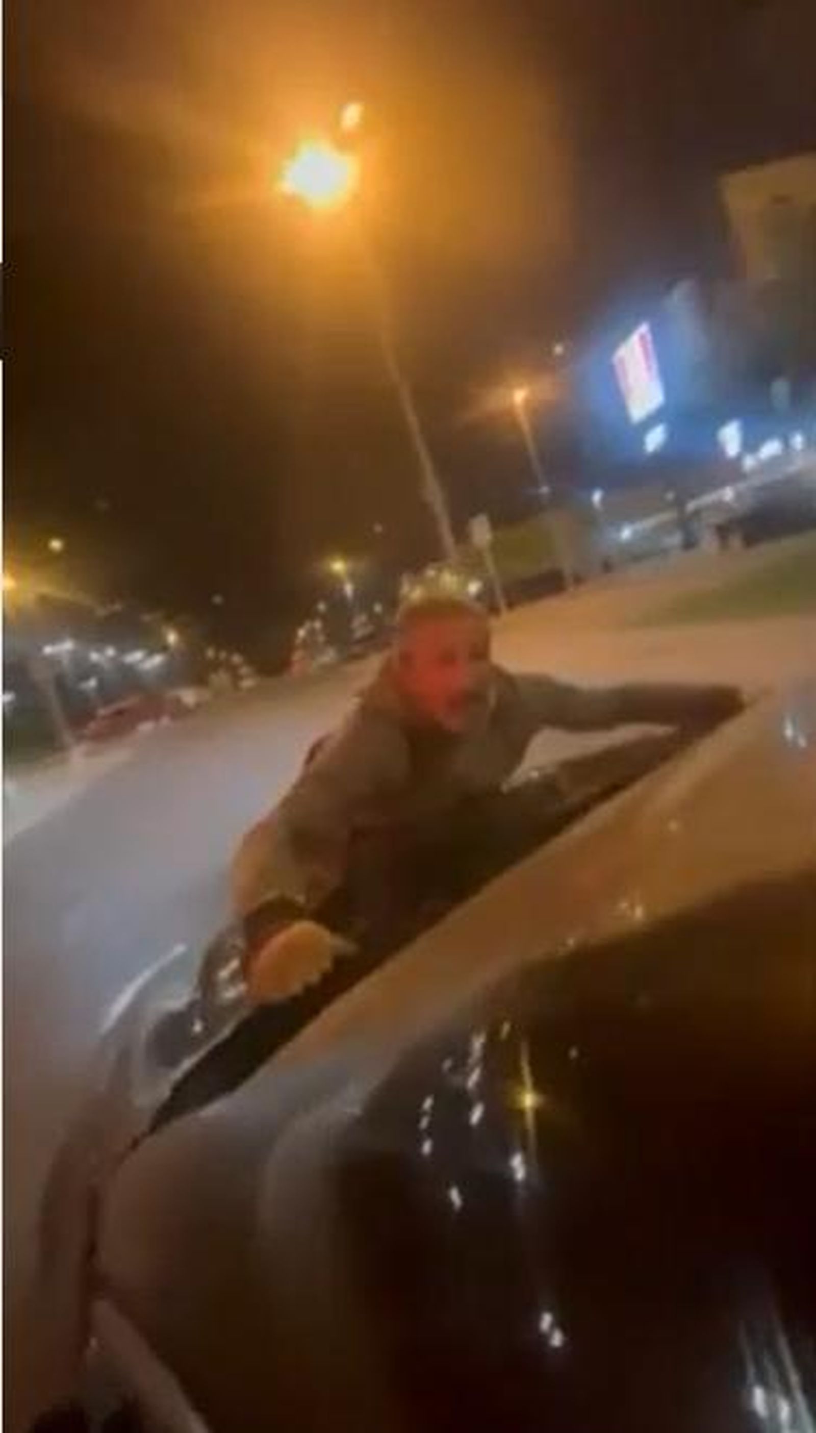 Un hombre sobre el capó de un coche a toda velocidad por las calles de Huelva.