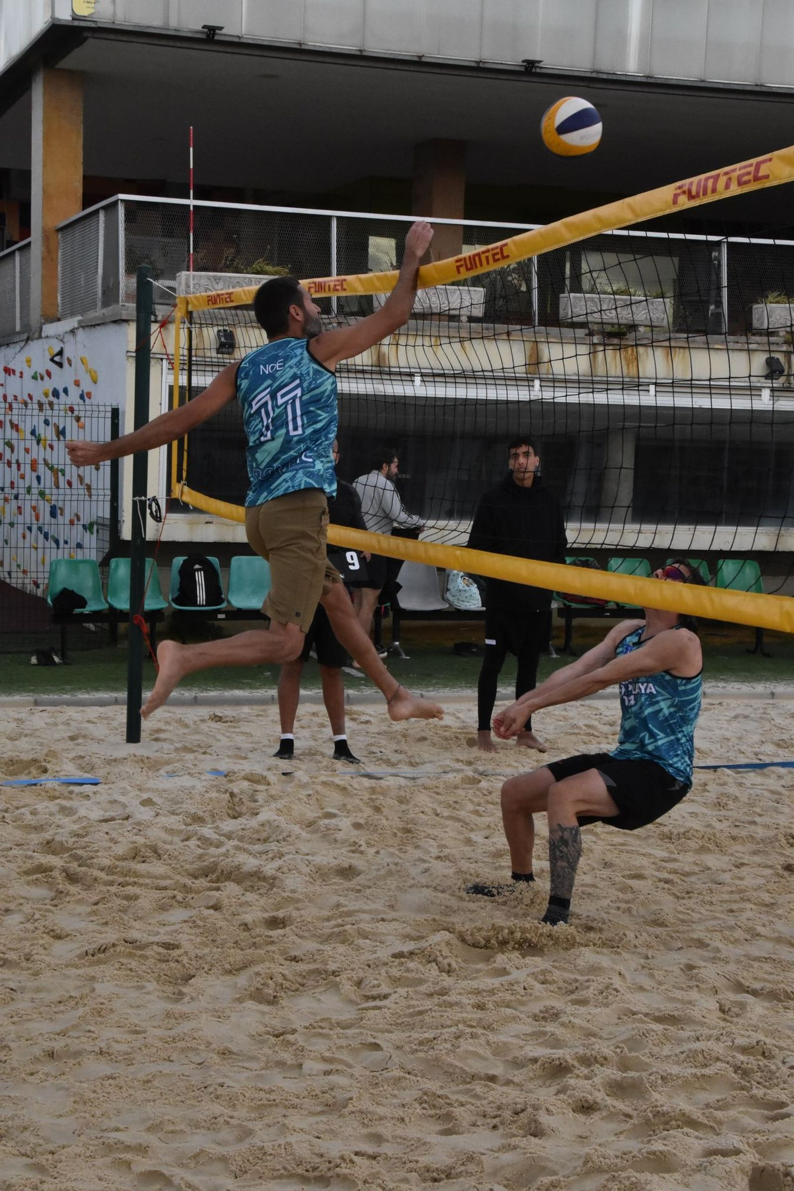 Momento de la competición de voley playa, con un remate en la red.