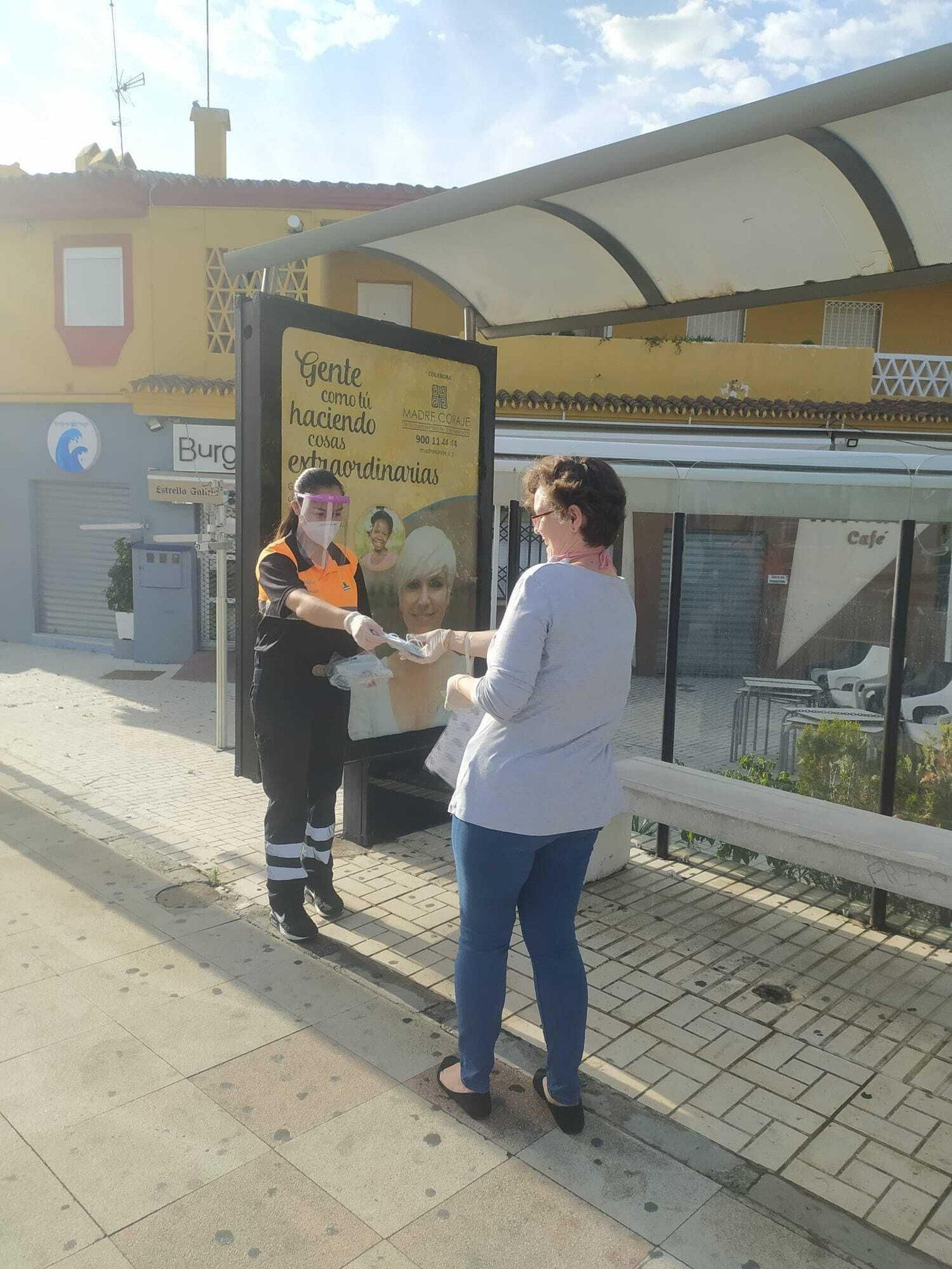 Una voluntaria de Protección Civil entrega una mascarilla a una mujer en una parada del autobús de Rincón de la Victoria.