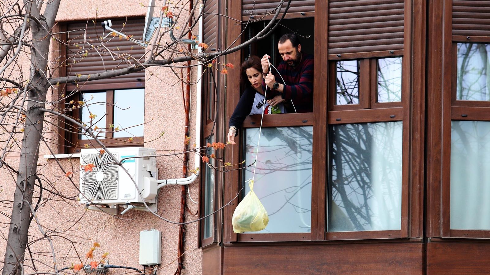 Una familia baja una bolsa con una cuerda por el confinamiento.