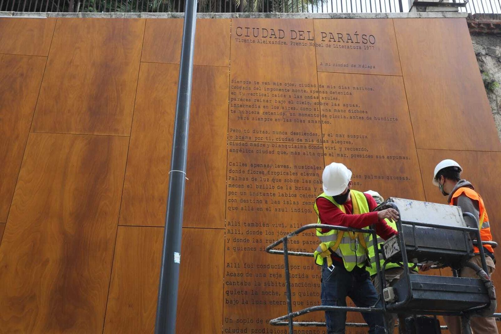 Los operarios tras colocar el poema 'Ciudad del Paraíso' de Vicente Aleixandre.