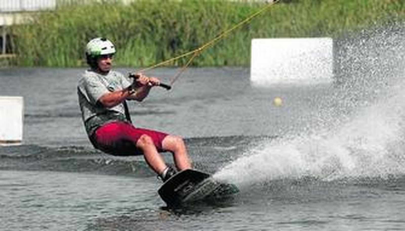 Un joven se desliza por el agua montado en una tabla y agarrado a las catenarias del cable esquí.