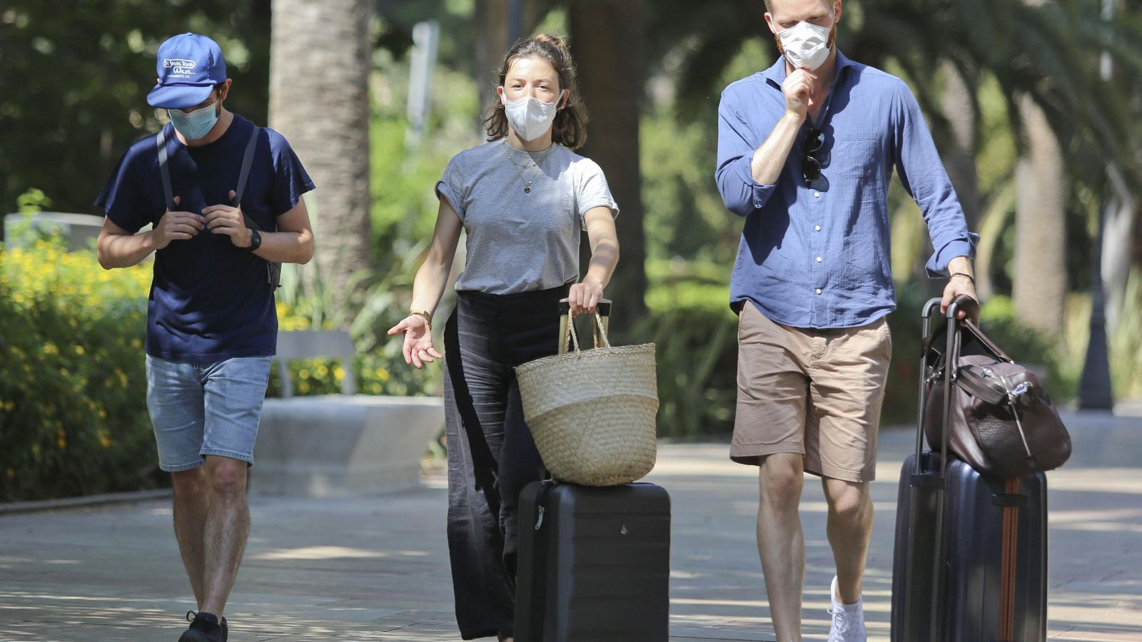 Varios turistas van por el parque de Málaga con sus maletas.