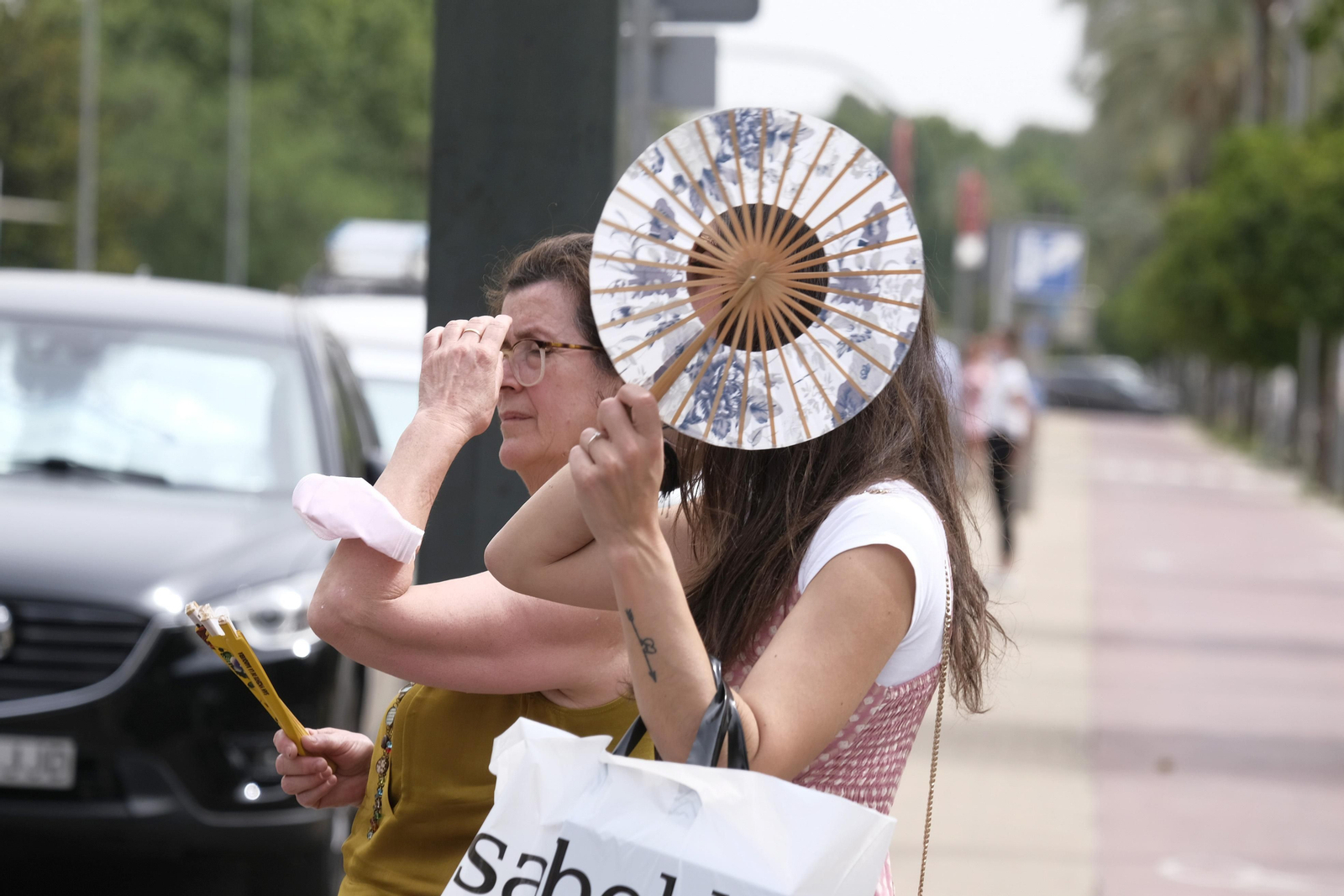 Dos personas caminan en Córdoba con sendos abanicos para refrescarse por el calor.