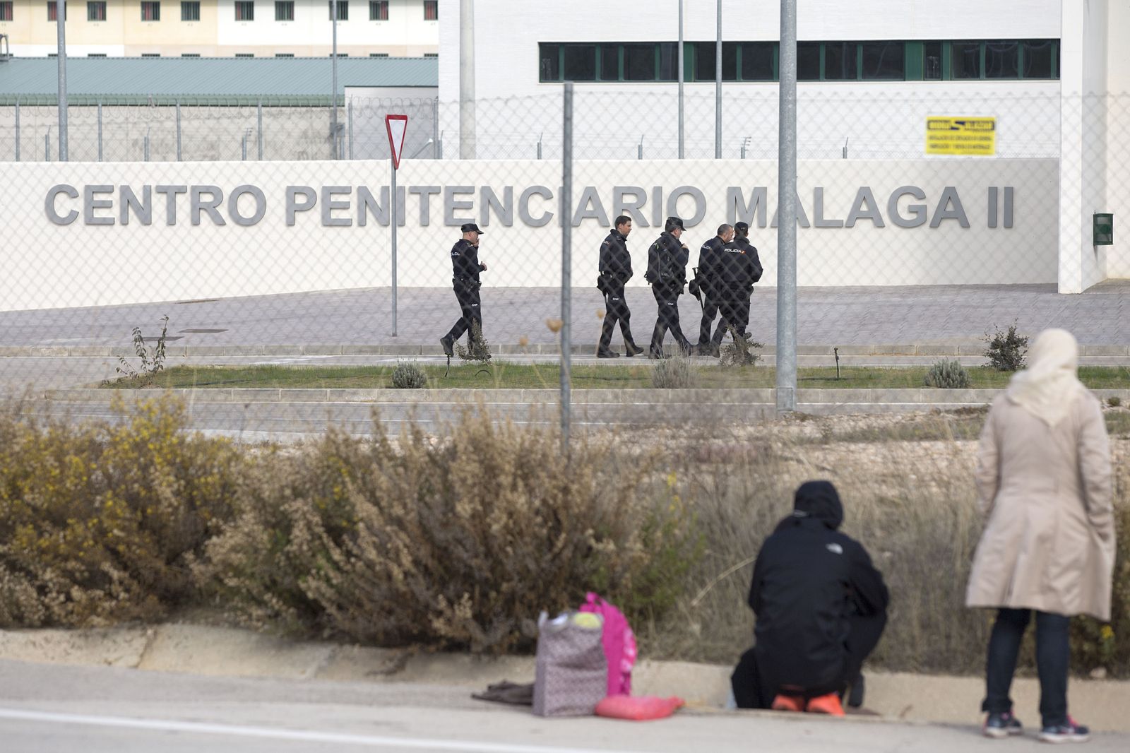Policías pasan delante de la cárcel de Archidona mientras familiares de los inmigrantes esperan para visitarlos.