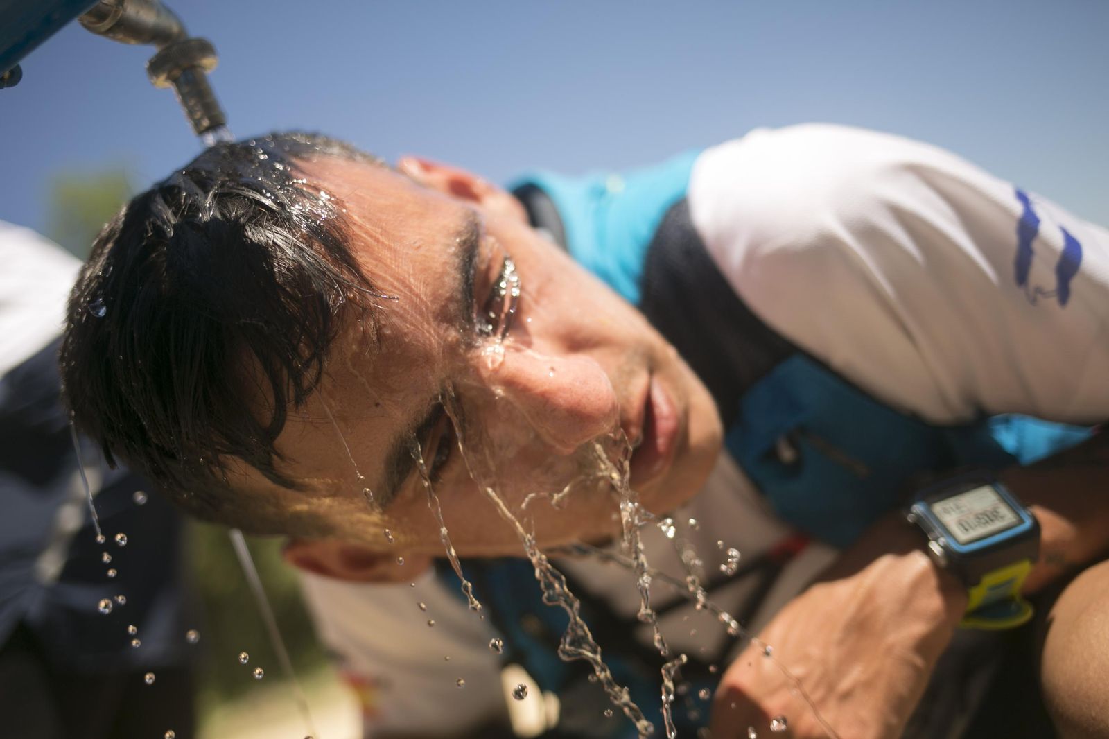 Un joven refrescándose en una fuente pública.