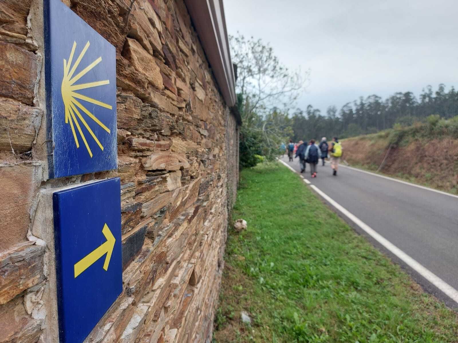 Detalle de una de las señales que indican el Camino  de Santiago , con los peregrinos al fondo.