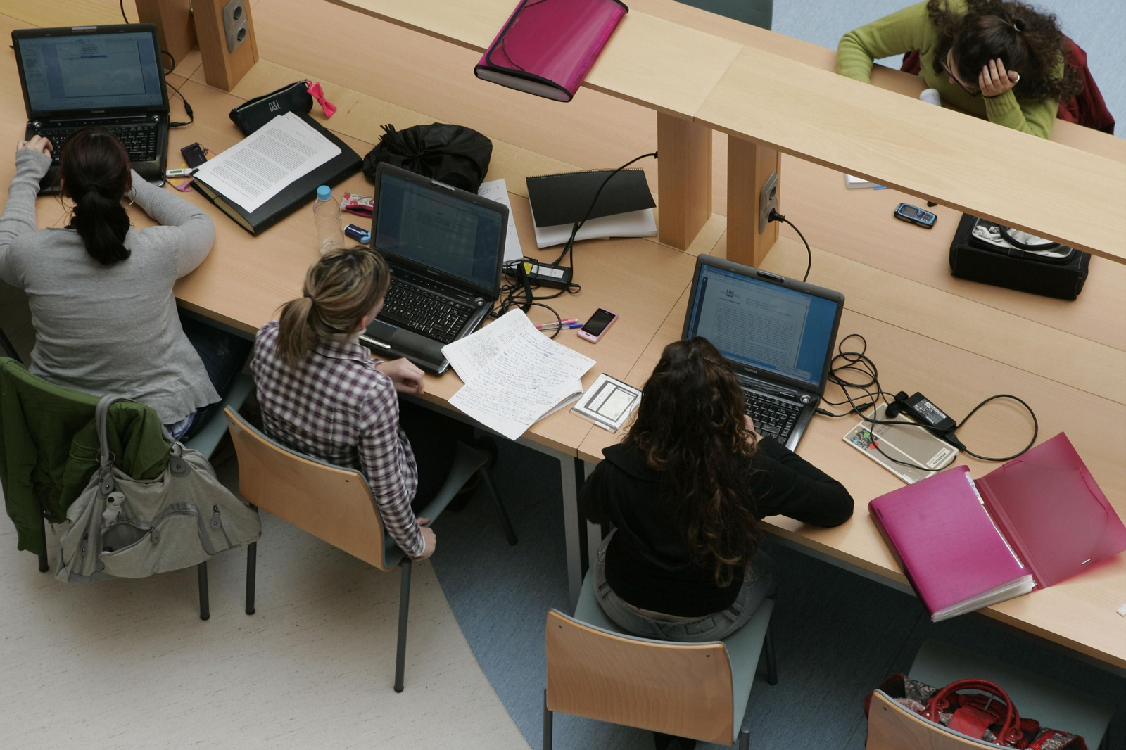 Alumnas con ordenadores portátiles en una biblioteca universitaria.