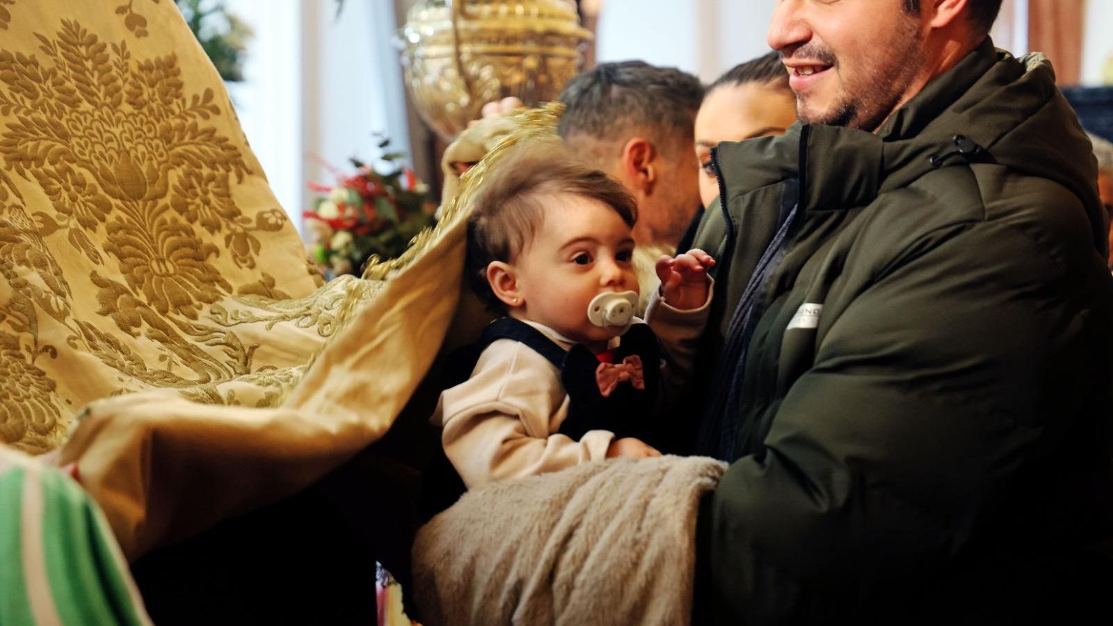 Un padre coloca a su bebé bajo el manto de la Virgen.