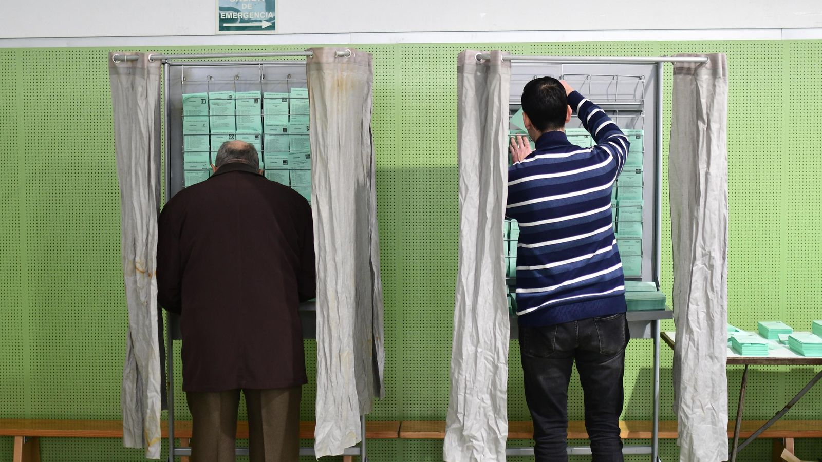 Dos personas cogen las papeletas para votar en un colegio electoral de la capital.