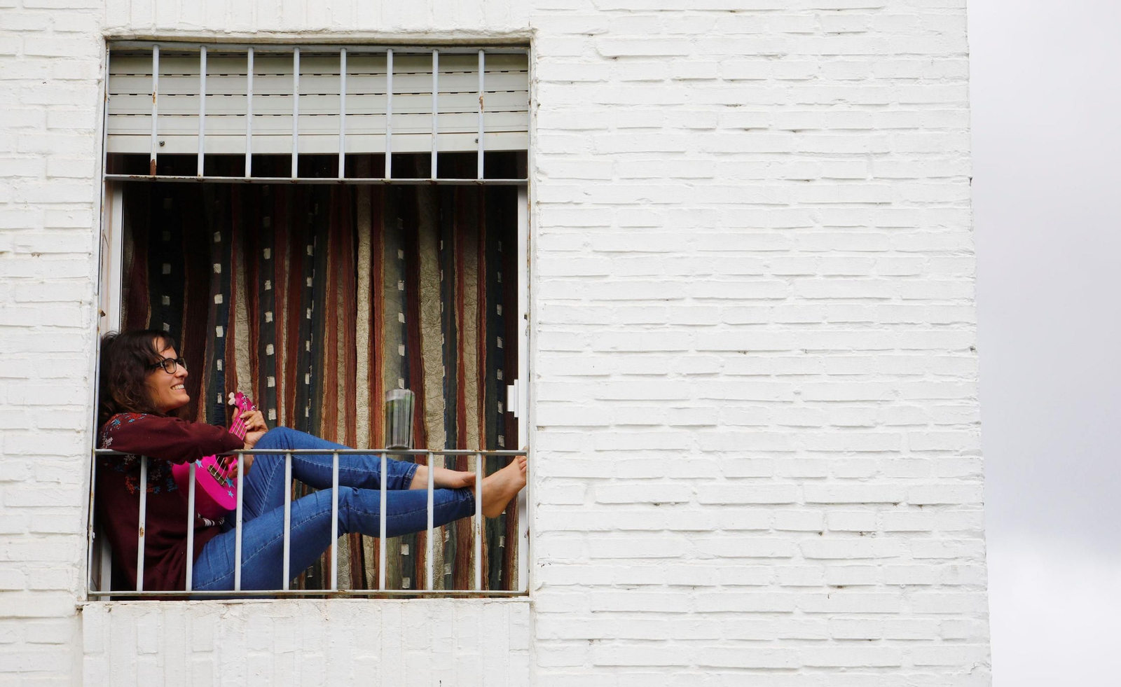 Una joven toca una guitarra sentada en la ventana de su vivienda en Córdoba.