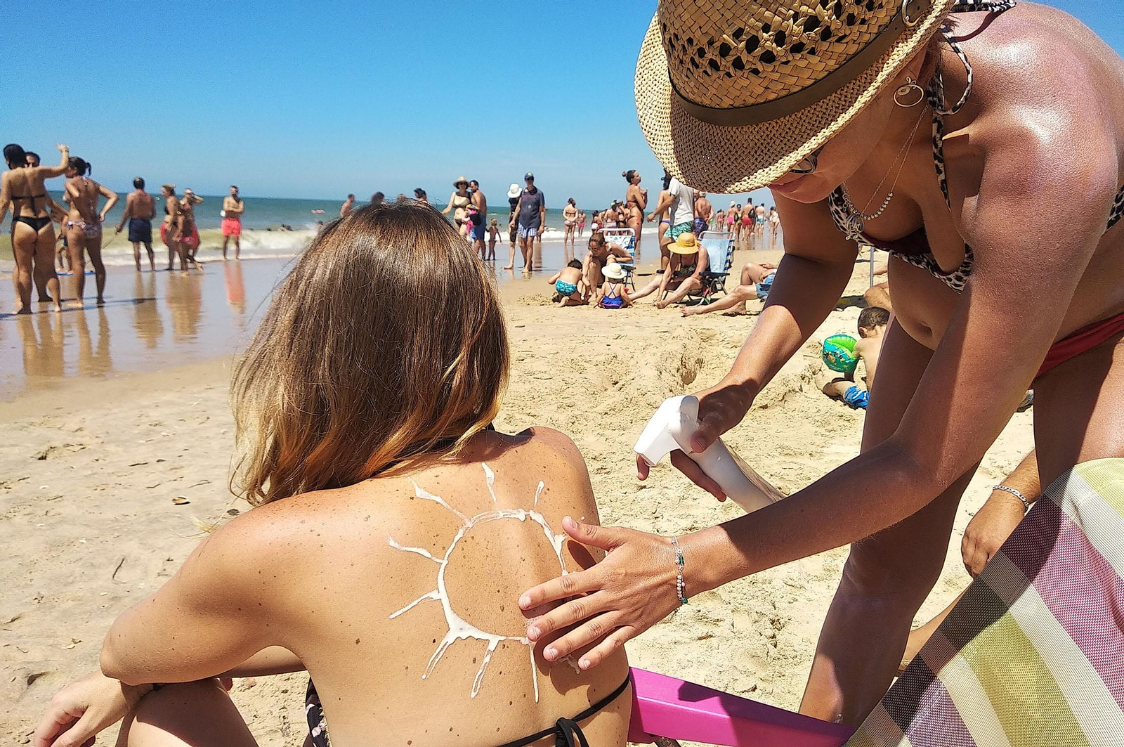 Una mujer echándole crema solar en la espalda a otra mujer para protegerse del sol durante una jornada en la playa.