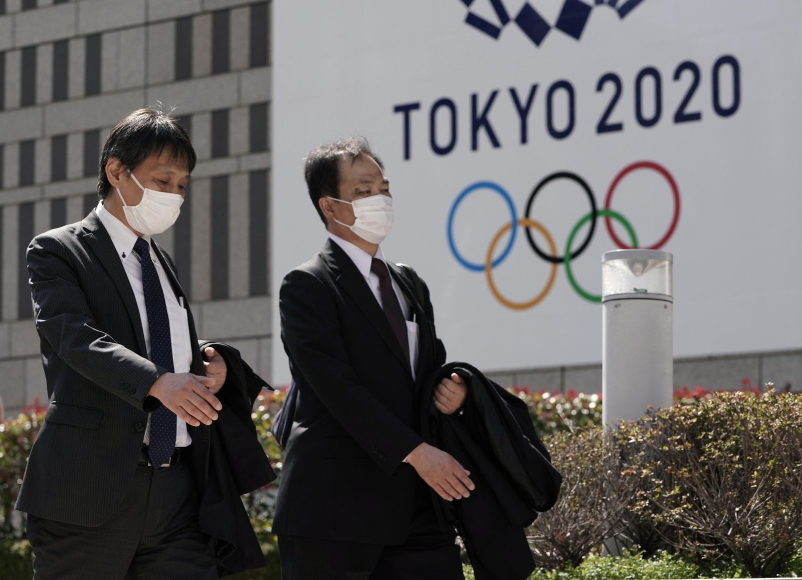 Dos japoneses con mascarillas pasan ante un cartel anunciando los JJOO de Tokio
