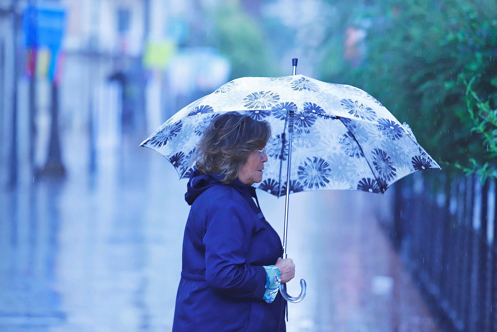 Una mujer se protege de la lluvia con su paraguas en una céntrica calle de Huelva