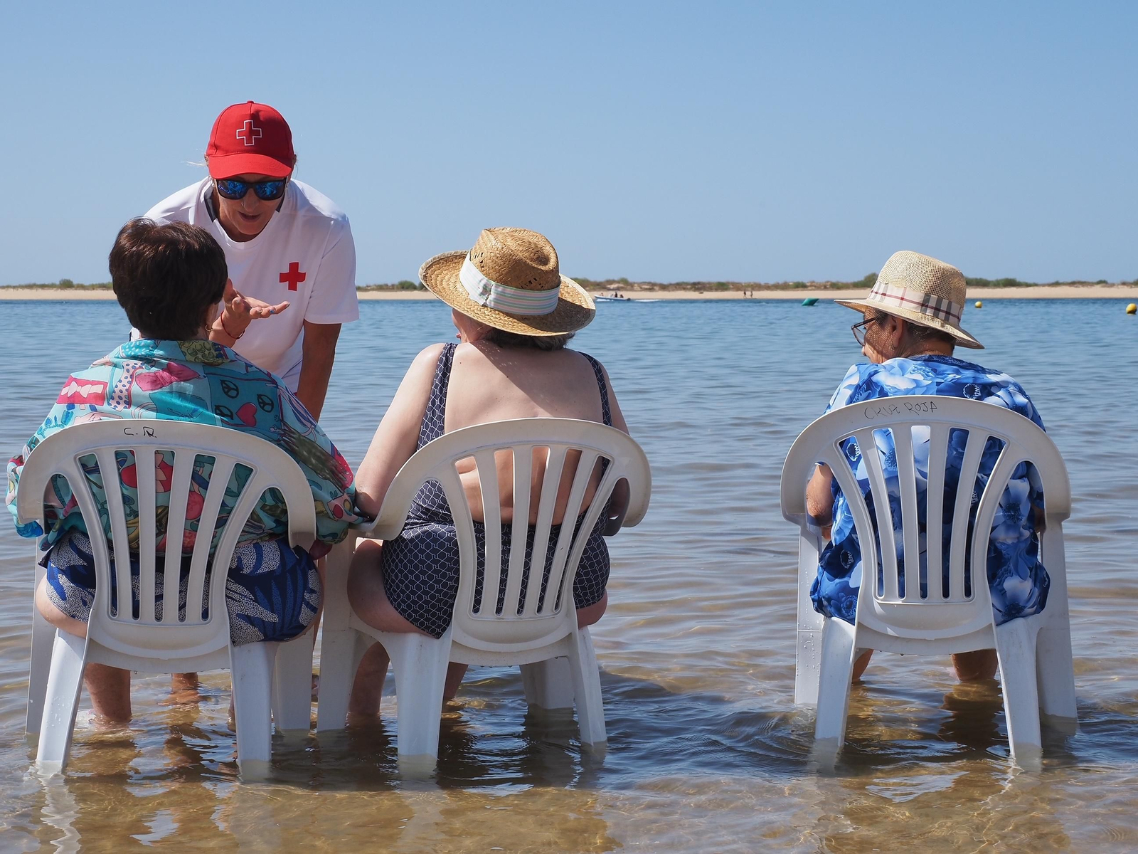 Una voluntaria de Cruz Roja conversa con varias usuarias del programa, en la misma orilla de la playa Una voluntaria de Cruz Roja conversa con varias usuarias del programa, en la misma orilla de la playa
