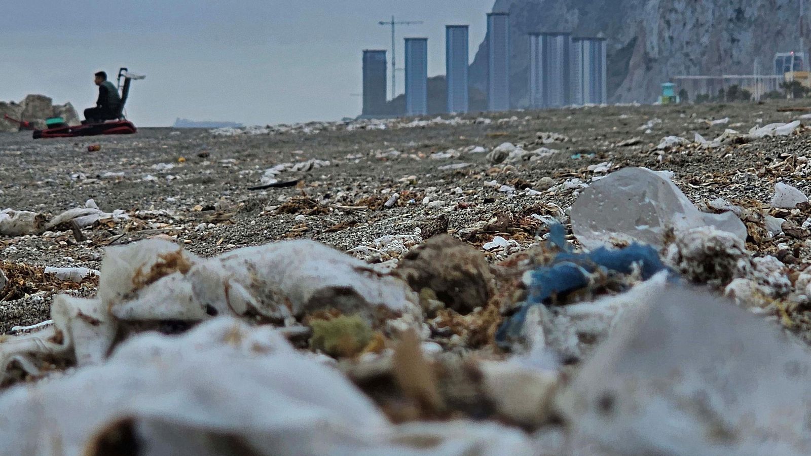 Toallitas y otros residuos sólidos en la playa de Levante de La Línea y, de fondo, las nuevas torres Hassan en Gibraltar.