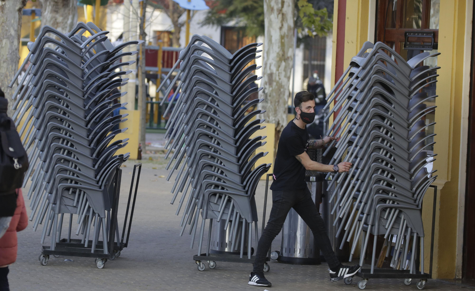 Un camarero recoge las sillas de un bar en Sevilla al cierre de por la tarde.