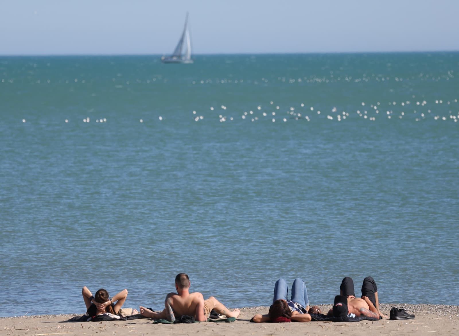 Un grupo de jóvenes toma el sol en una playa de Málaga capital.