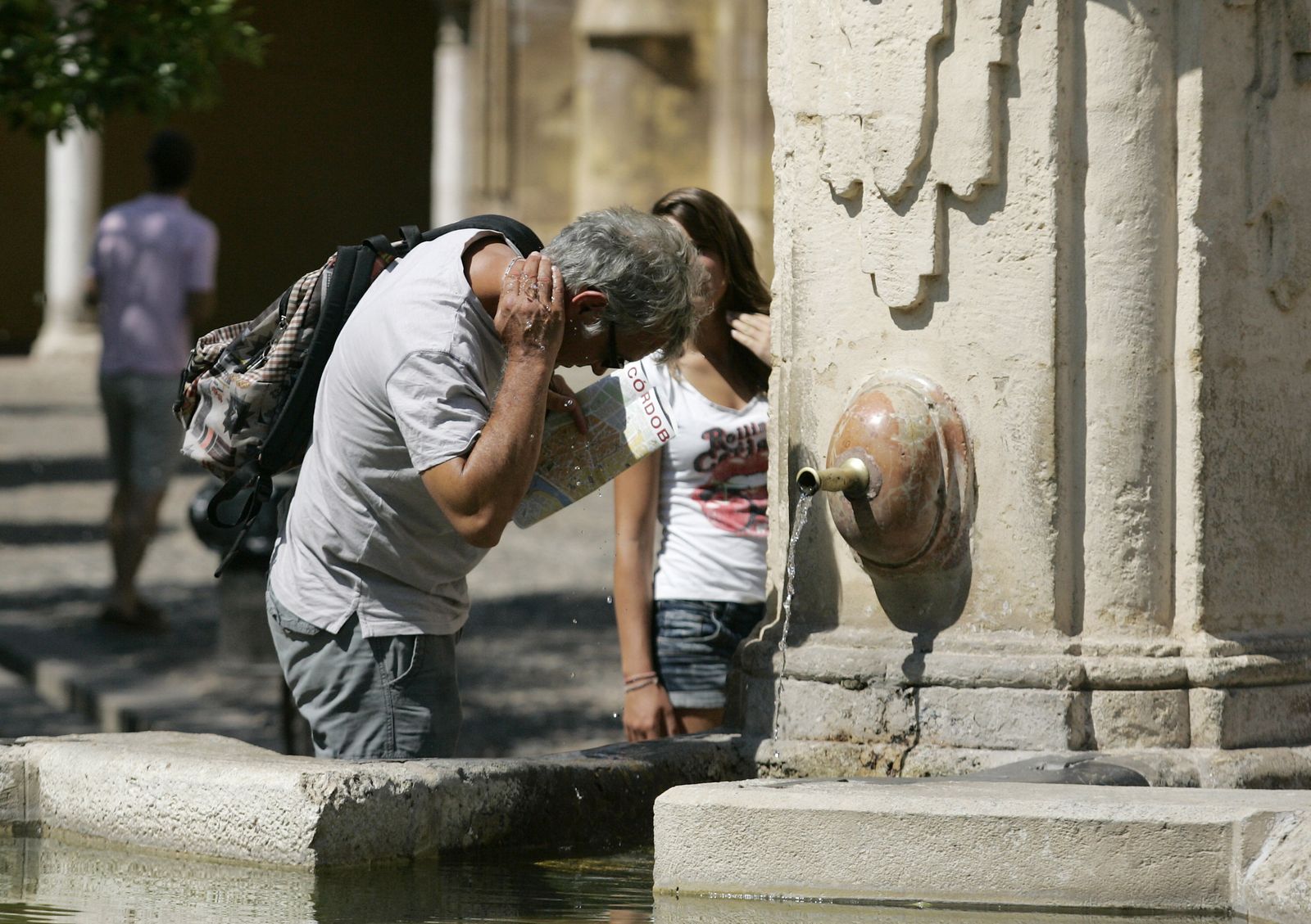Turistas se refrescan en la fuente del Patio de los Naranjos.