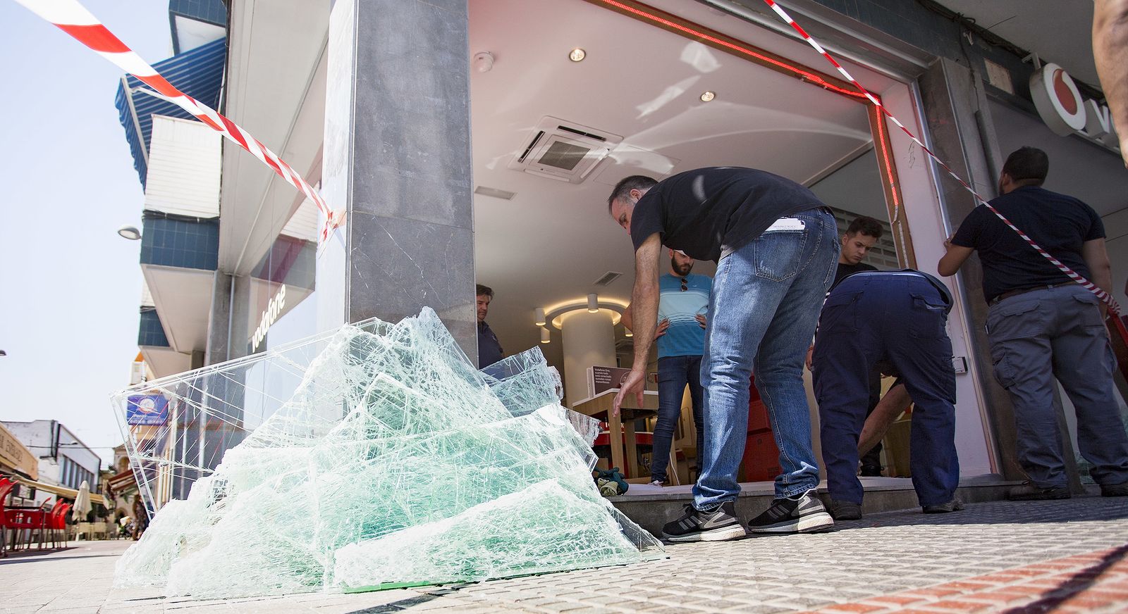 Unos operarios retiran los cristales rotos de la tienda.