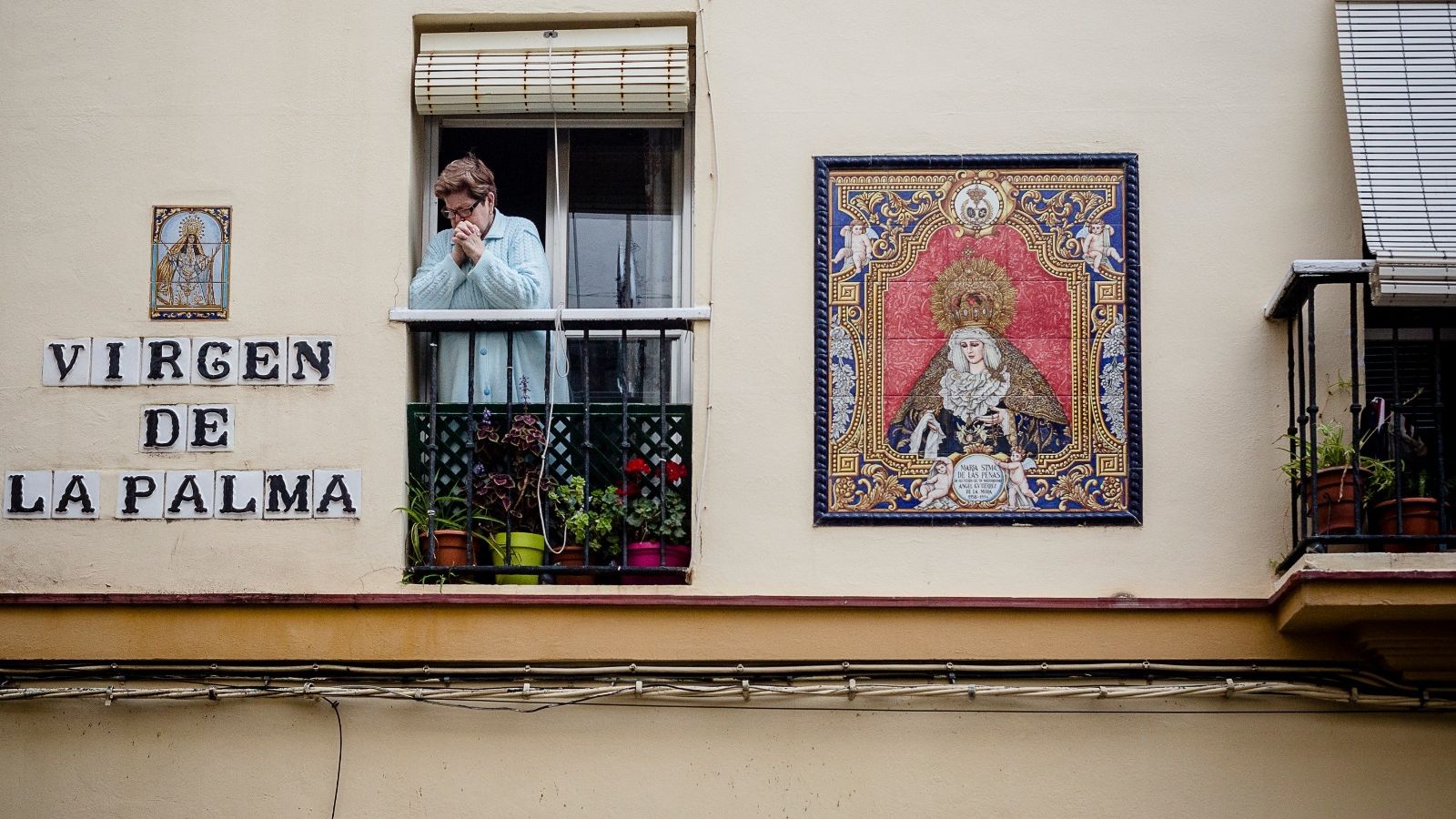 Una mujer sigue el rezo del rosario desde su balcón junto a la Iglesia de La Palma.