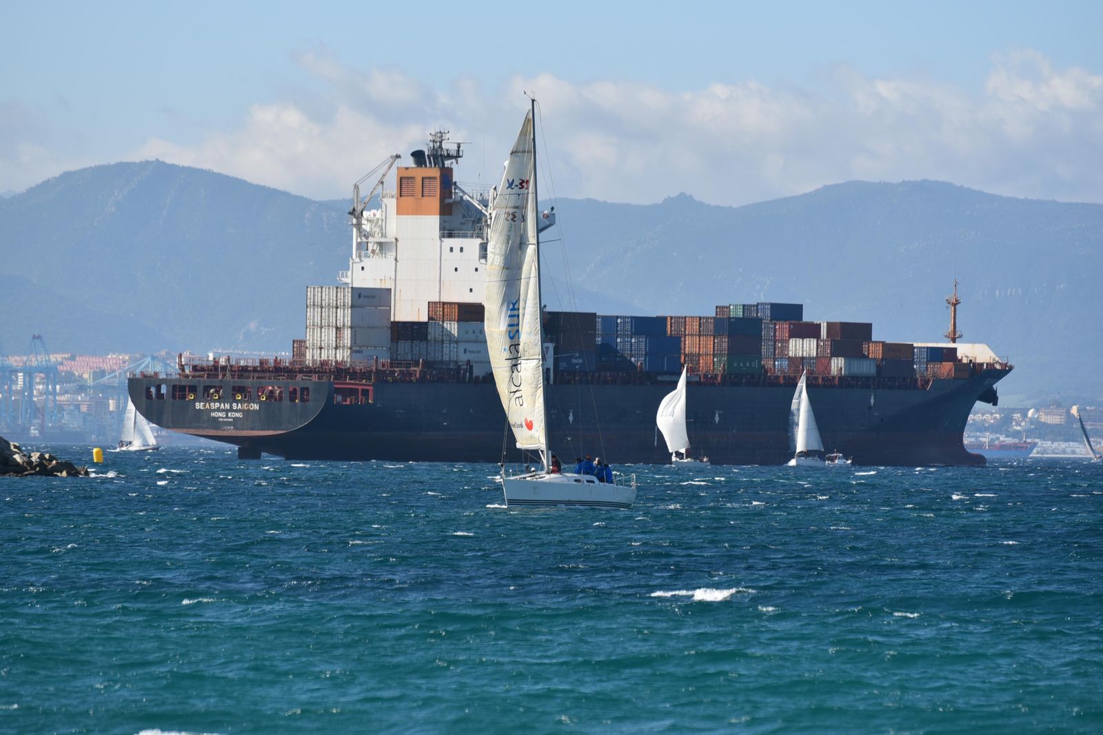 Buque portacontenedores rodeado de veleros frente a la  playa de  poniente en La Línea