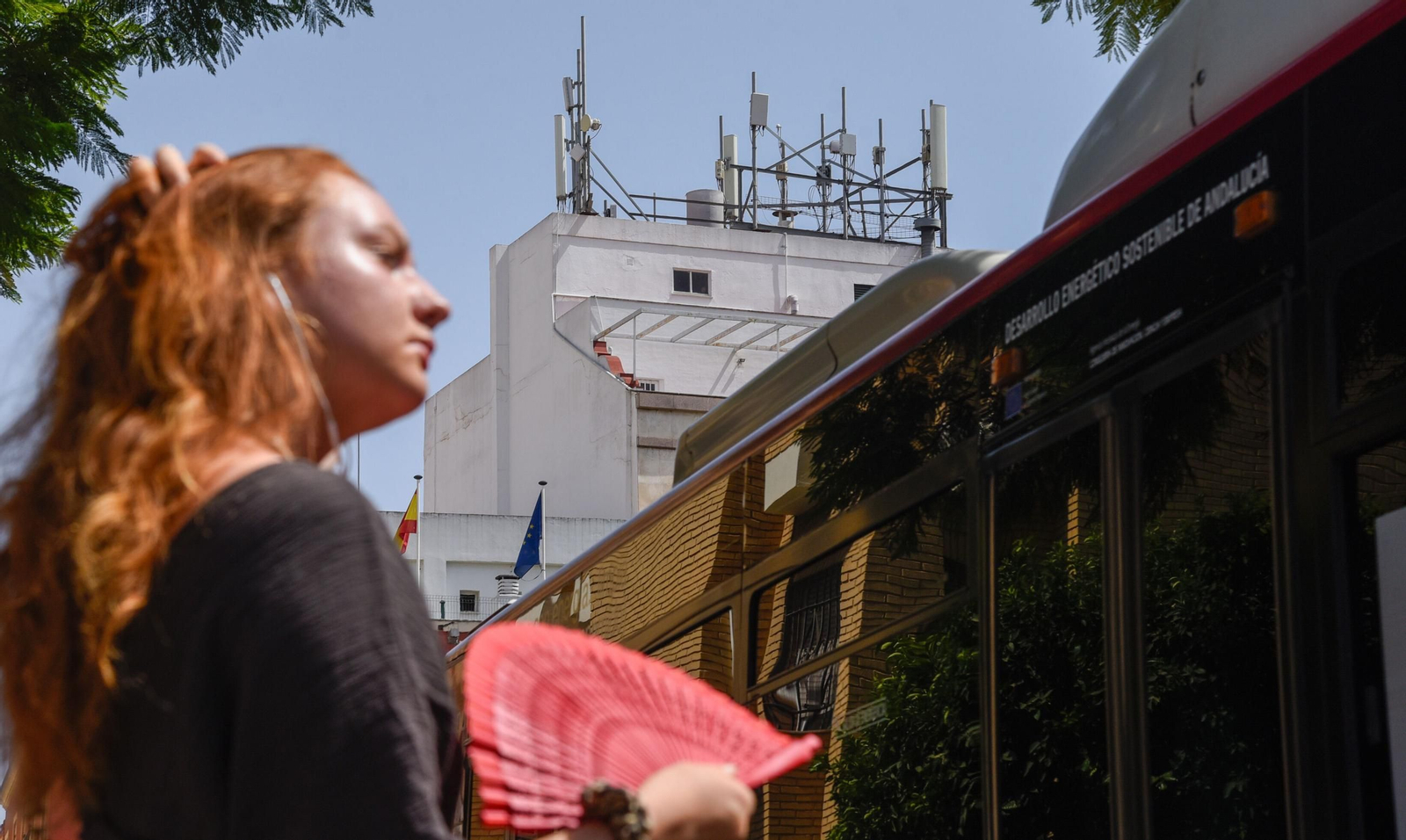 Una mujer se abanica al paso de un autobús de Tussam por la plaza Padre Jerónimo de Córdoba. Al fondo, varias antenas en una azotea.