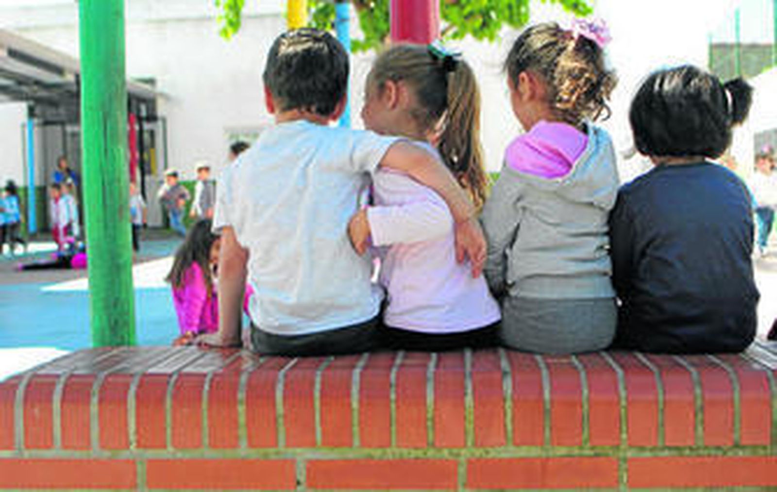 Varios alumnos sentados en un banco durante el recreo observan a sus compañeros.