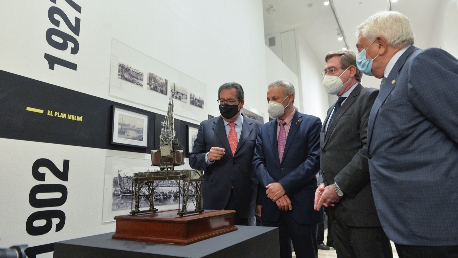 Pulido, Toledo, Carmona y Herrero observan la maqueta de una grúa del Puerto de Sevilla que se expone en la Fundación Cajasol.