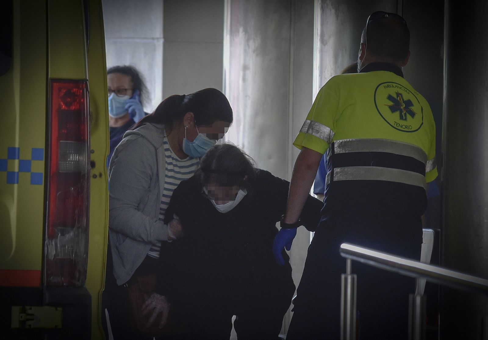 Una mujer mayor es ayudada por un familiar y los sanitarios a bajar de la ambulancia en las Urgencias del Macarena.