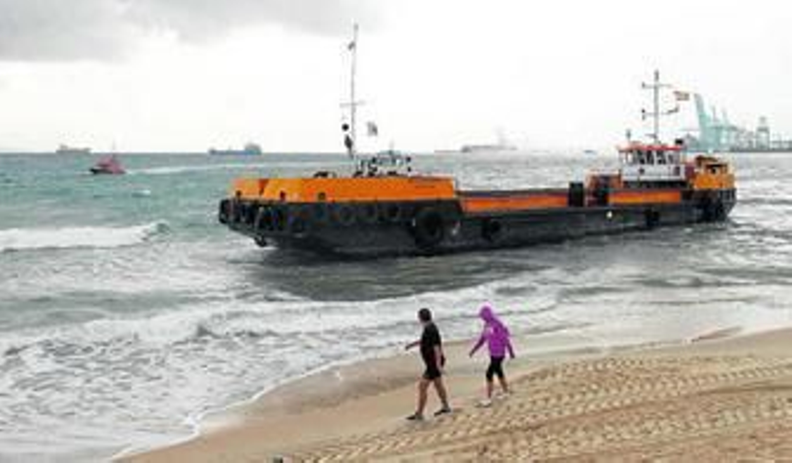 Dos personas observan el buque embarrancado mientras pasean por la playa del Rinconcillo, ayer por la mañana.