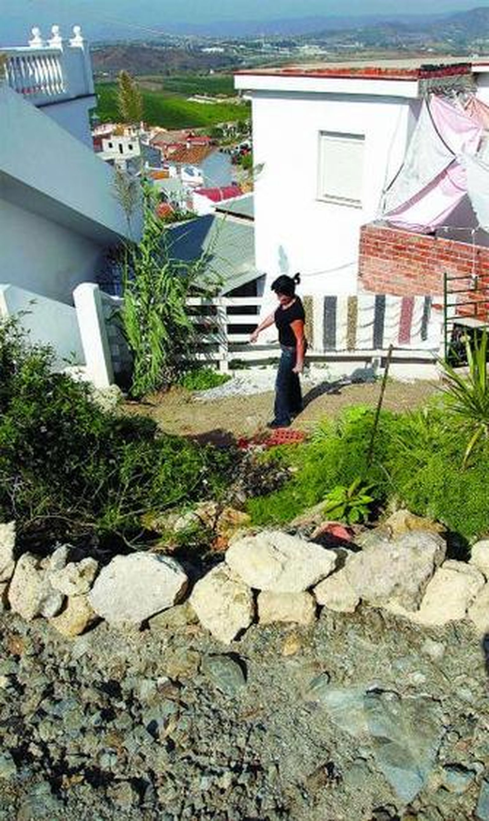 1. Una de las vecinas que vive en la cima de Colmenarejo Alto, junto a la entrada de su vivienda. 2. Una mujer anciana, vecina de esta barriada del distrito de Campanillas, ayer, subiendo una de las empinadas cuestas del vecindario. 3. Imagen del camino alternativo por donde deben subir los vehículos que quieran acceder a la zona alta del barrio. 4. Un turismo baja por el citado carril, sin asfaltar, lleno de boquetes y con distinto ancho según el tramo.