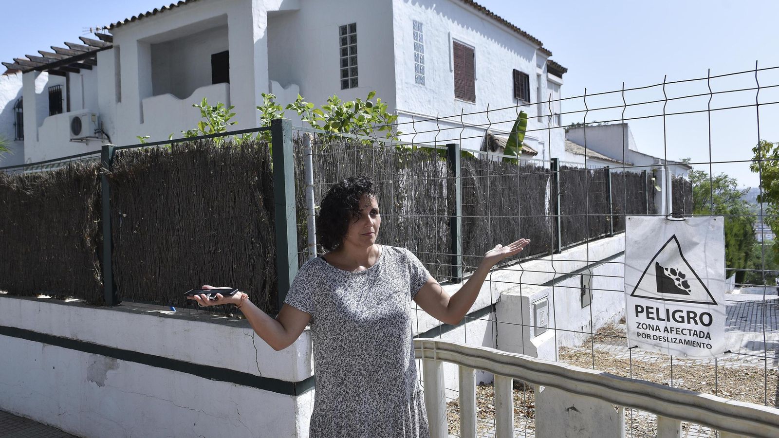 Una vecina, junto al cartel que acota la zona y alerta de que está "afectada por deslizamientos"